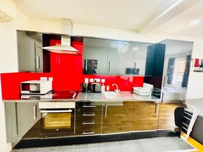 A modern kitchen with stainless steel appliances, a red accent wall, and a black countertop. - Cosy one bedroom flat near Aldgate East station (Greater London)