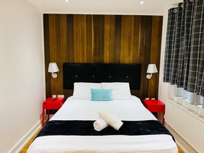 A hotel room with a large bed, two bedside tables, a black headboard, and a window with curtains. - Wonderful one bedroom apartment in Great location (Greater London)
