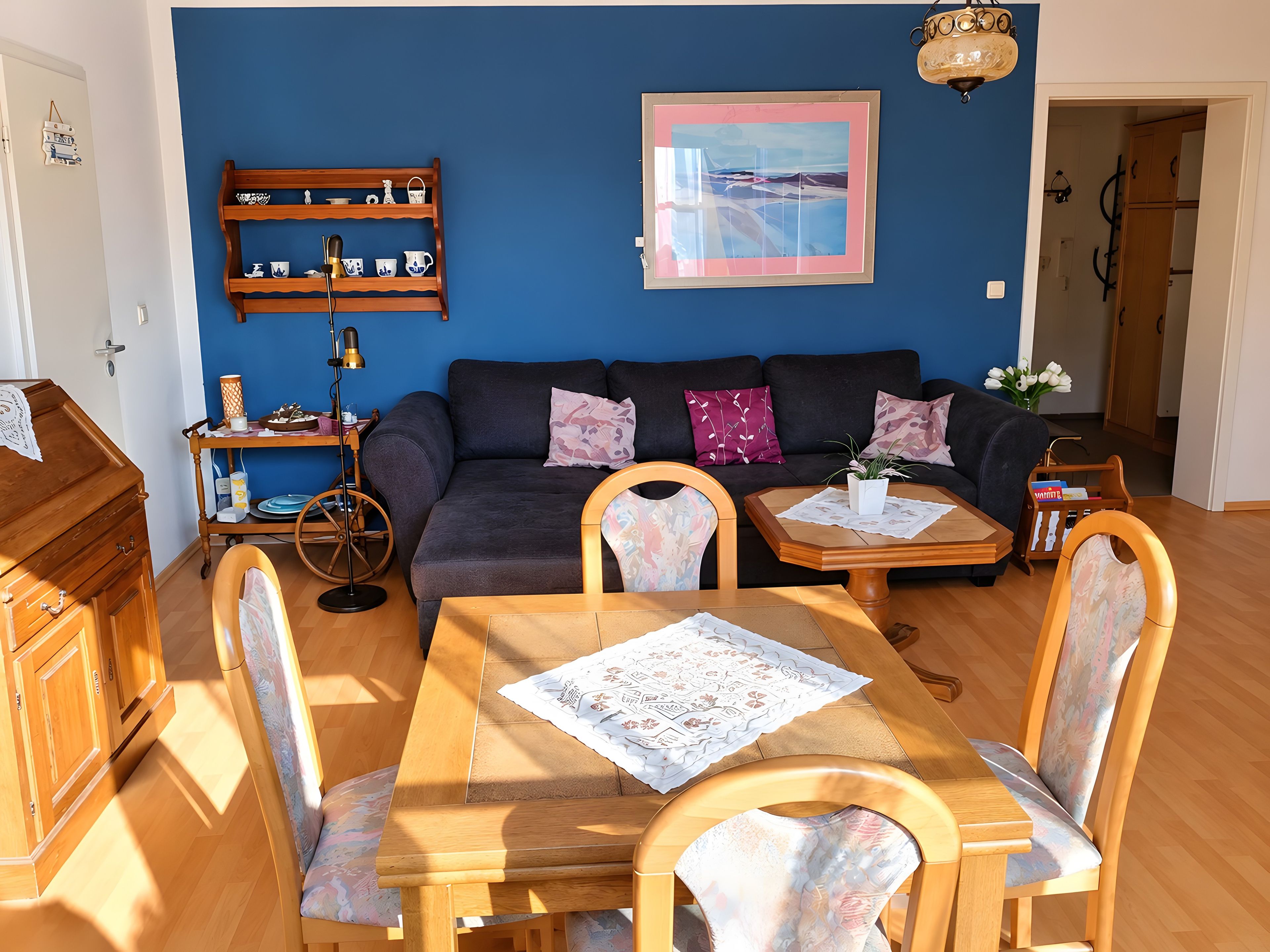 Un soggiorno con parete blu, un divano, un tavolino da caffè, un tavolo da pranzo con sedie, un mobiletto in legno e una mensola con oggetti decorativi.