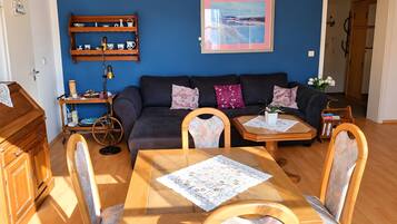 Un soggiorno con parete blu, un divano, un tavolino da caffè, un tavolo da pranzo con sedie, un mobiletto in legno e una mensola con oggetti decorativi.