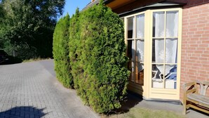Ein Gebäude mit Ziegelaußenwand, einem großen Fenster mit weißem Vorhang und einem ordentlich geschnittenen Heckenstreifen.