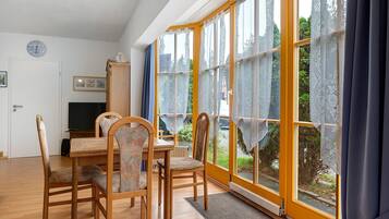 Ein Essbereich mit Tisch, Stühlen, einem Fernseher und einem Fenster mit Spitzenvorhängen.