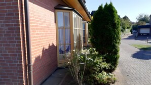 Ein Backsteinhaus mit einem Fensterzugang, einer kleinen Grünfläche und einem gepflasterten Auffahrtsweg.