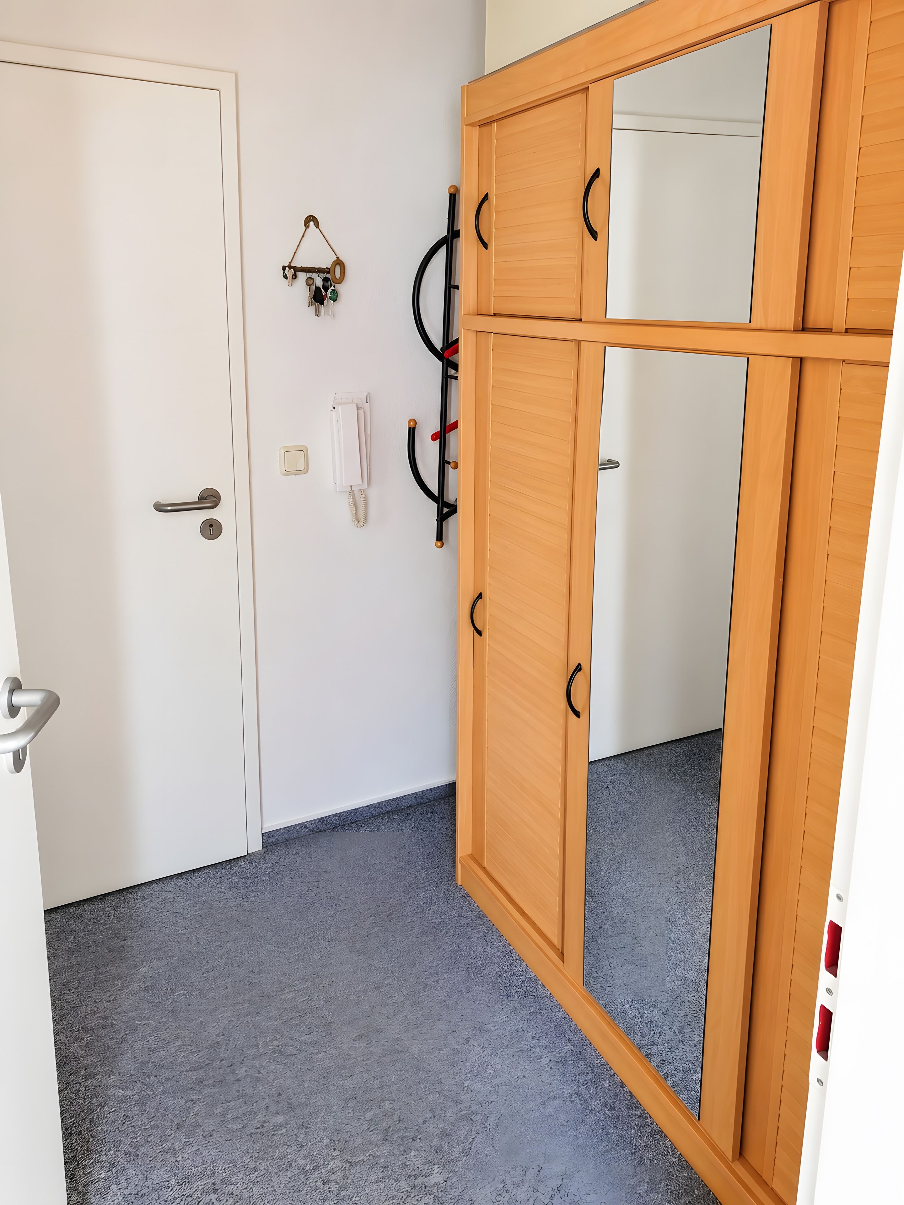 Ein Zimmer mit einer weißen Tür, einem Holzschrank mit schwarzen Griffen, einem Telefon und einem Kleiderständer.