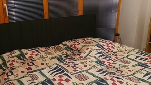A bed with a patterned quilt, a dark headboard, and blinds on the windows. - Apartment at Schönberger Strand – Just 200 Meters from the Beach (Schönberg)
