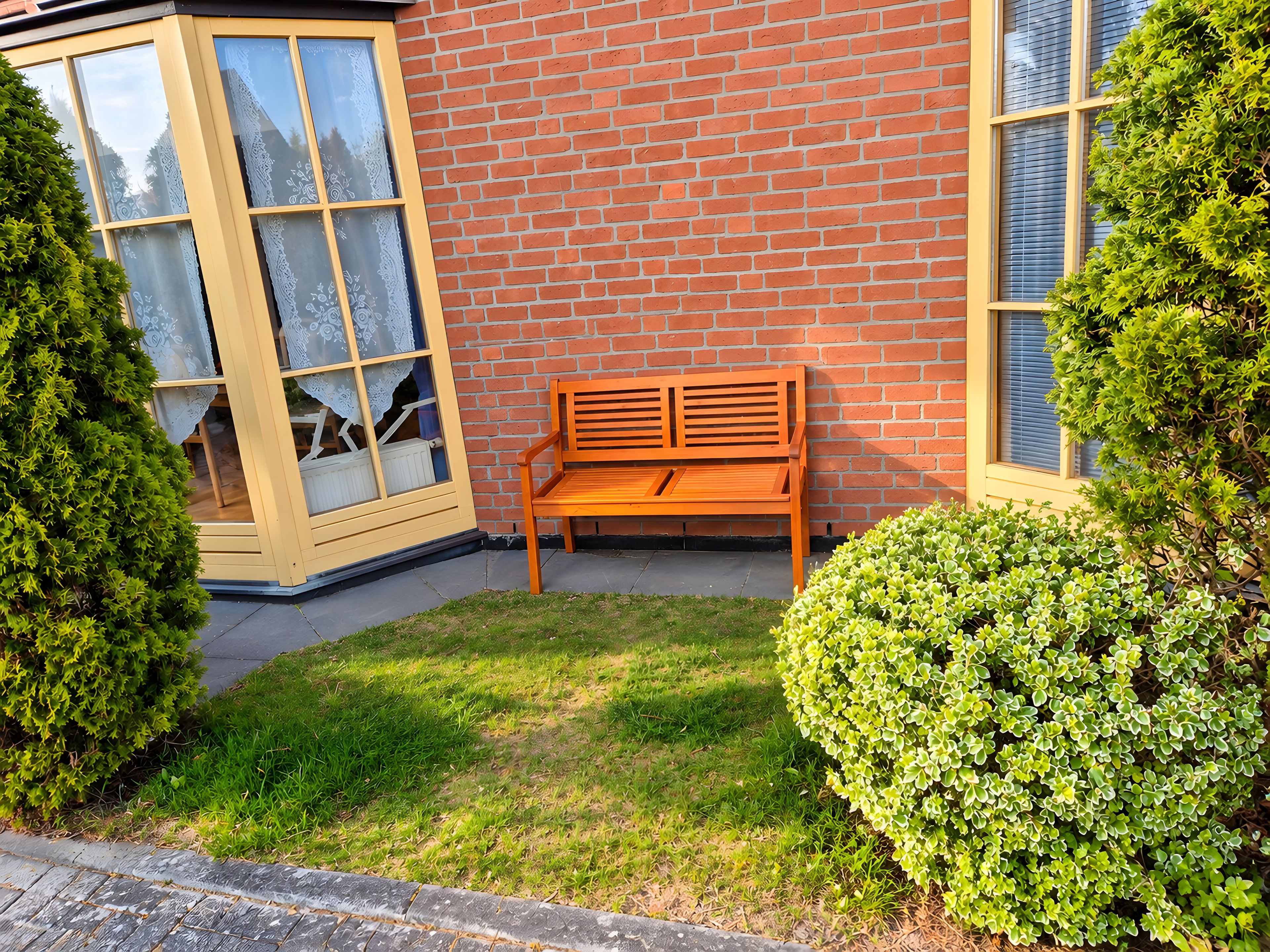 Eine hölzerne Bank vor einem Backsteinhaus mit Fenster und Tür.