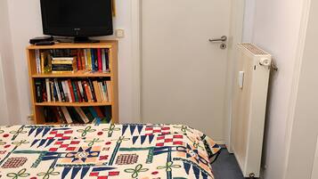 Una camera da letto con un letto, una libreria, un televisore, una porta e un termosifone.