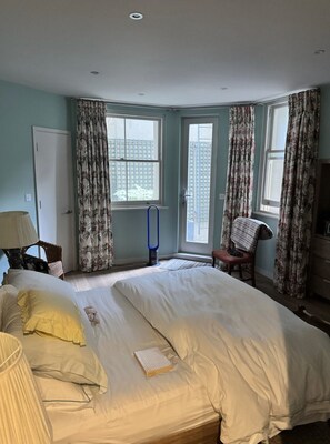 Ein Schlafzimmer mit einem großen Bett, einem Sessel, einem Schreibtisch und einem Fenster mit Vorhängen.