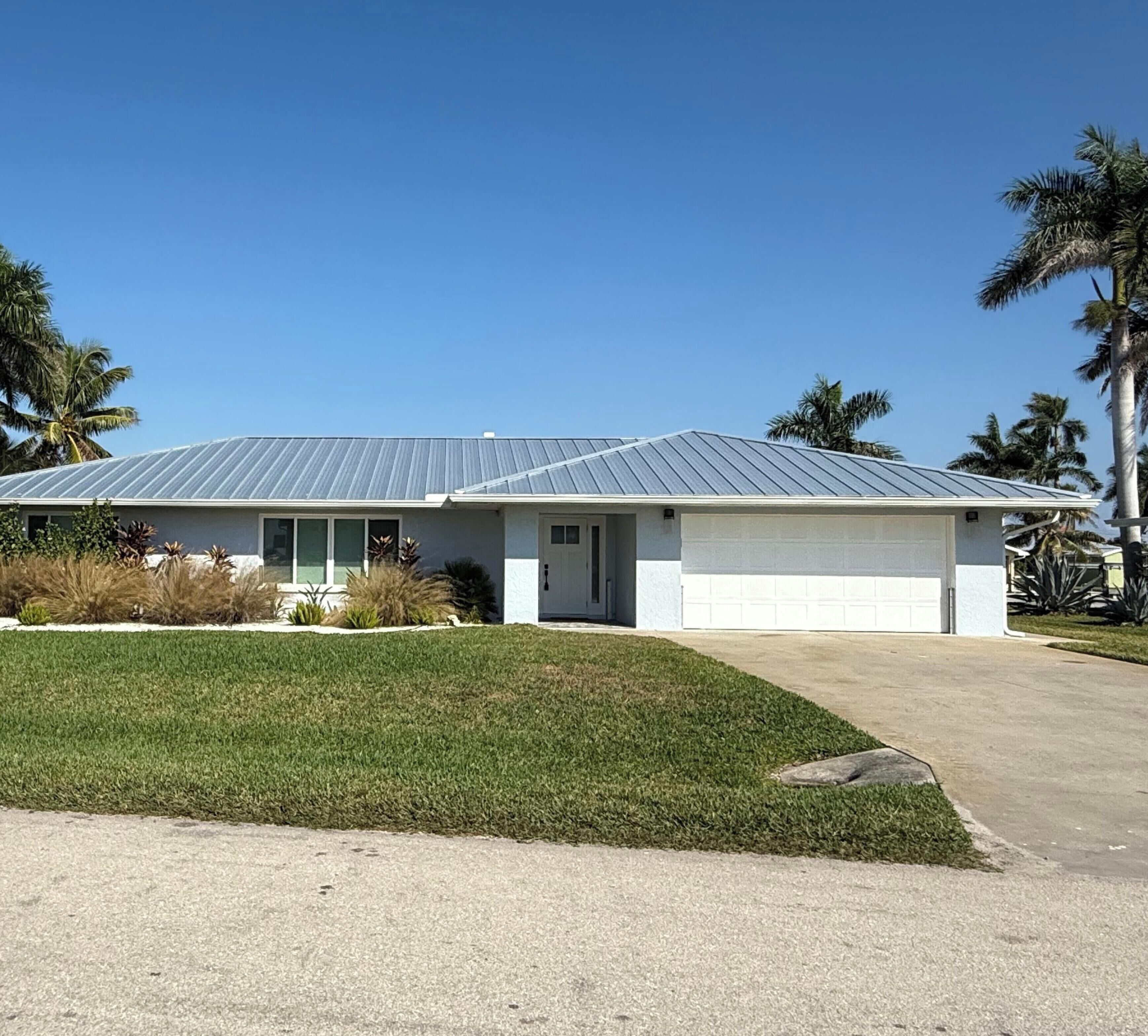 A single-story house with a garage, surrounded by a well-maintained lawn and palm trees.