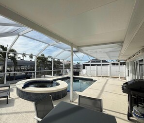 Ein Außenpoolbereich mit Whirlpool, überdachter Lounge und Grill.