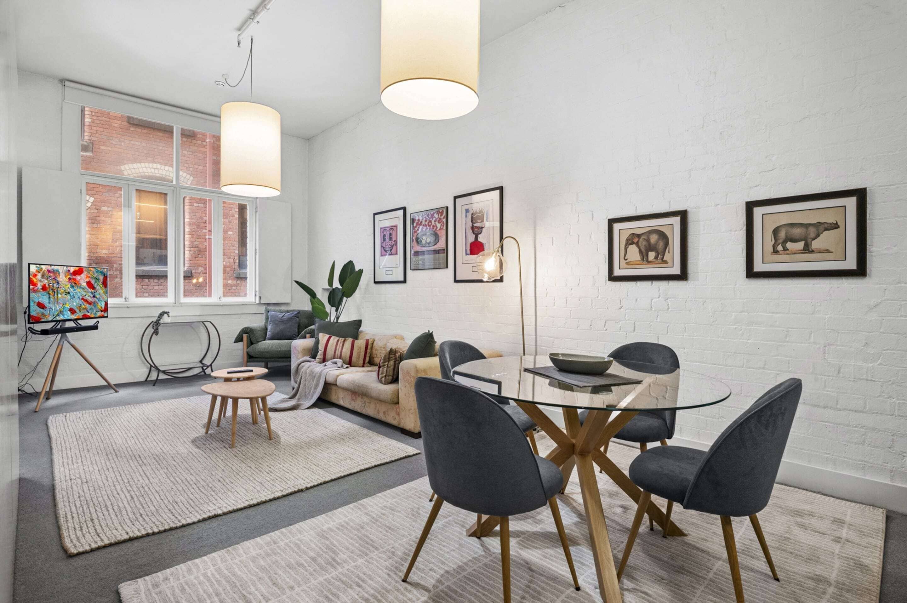 Un salon moderne comprenant un canapé, une table à manger, des chaises, des œuvres d’art accrochées au mur et une grande fenêtre.