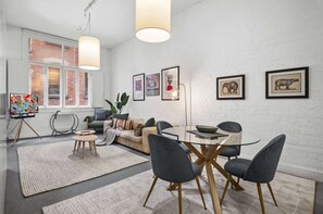 Ein modernes Wohnzimmer mit einer Couch, einem Esstisch, Stühlen, Kunstwerken an der Wand und einem großen Fenster.