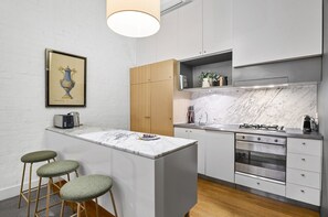Eine moderne Küche mit Marmorarbeitsplatte, Edelstahlgeräten, Holzschränken und einem gerahmten Kunstwerk an der Wand.
