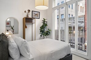 A bedroom with a bed, a mirror, a plant, a shelf with decorative items, and a view through a large window. - Chic 2-bed Apartment in Melbourne CBD (Melbourne)