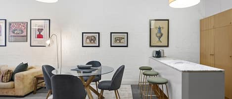 A modern kitchen with a white brick wall, a round dining table with chairs, a bar area with stools, and framed pictures on the wall.