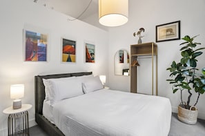 Ein ordentlich eingerichtetes Hotelzimmer mit Bett, Nachttischlampen, einem Spiegel, Wandbildern und einer Topfpflanze.