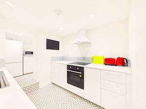 A modern kitchen with white cabinets, a black oven, a microwave, and a red kettle. - London Road Apartment | Modern | Parking (Gloucestershire)
