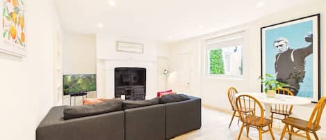 A modern living room with a sectional sofa, a fireplace, a dining area with wooden chairs, and a television.