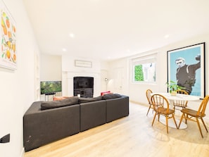 A modern living room with a sectional sofa, a fireplace, a dining area with wooden chairs, and a television. - London Road Apartment | Modern | Parking (Gloucestershire)