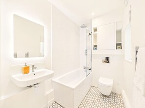 Een moderne badkamer met een witte wastafel, een bad, een toilet en een douche met glazen wanden.