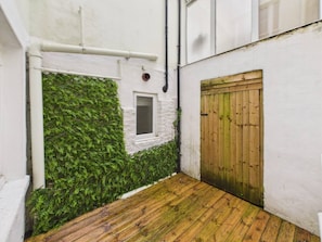 A narrow alleyway with a wooden door, a window, and a wall covered in green foliage. - London Road Apartment | Modern | Parking (Gloucestershire)