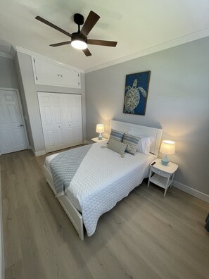 Ein Schlafzimmer mit einem Bett, zwei Nachttischen mit Lampen, einem Deckenventilator, einem Wandbild und einem Kleiderschrank.