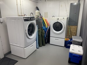 Ein Waschraum mit zwei übereinander gestapelten Waschmaschinen und Trocknern, einem Boiler und verschiedenen Reinigungsmitteln.