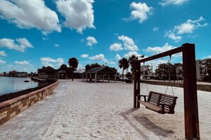 A beach with a wooden swing, a covered pavilion, and a body of water in the background. - The Gulf Oasis-
 Pool, hot tub, boat ramp, floating dock, kayaks, waterfront (Hudson)