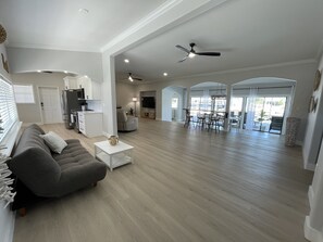 Ein geräumiger Wohnbereich mit grauem Sofa, weißem Couchtisch und einer Küche im Hintergrund.