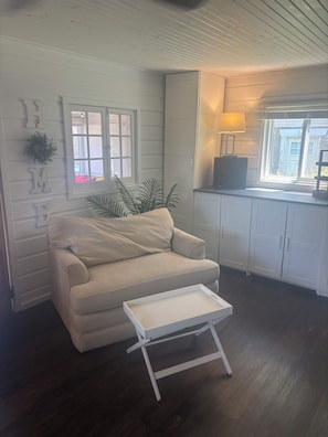 Ein Wohnzimmer mit einem beigefarbenen Sofa, einem kleinen weißen Tisch, einem Fenster mit Blick und einem Schrank mit einer Lampe.