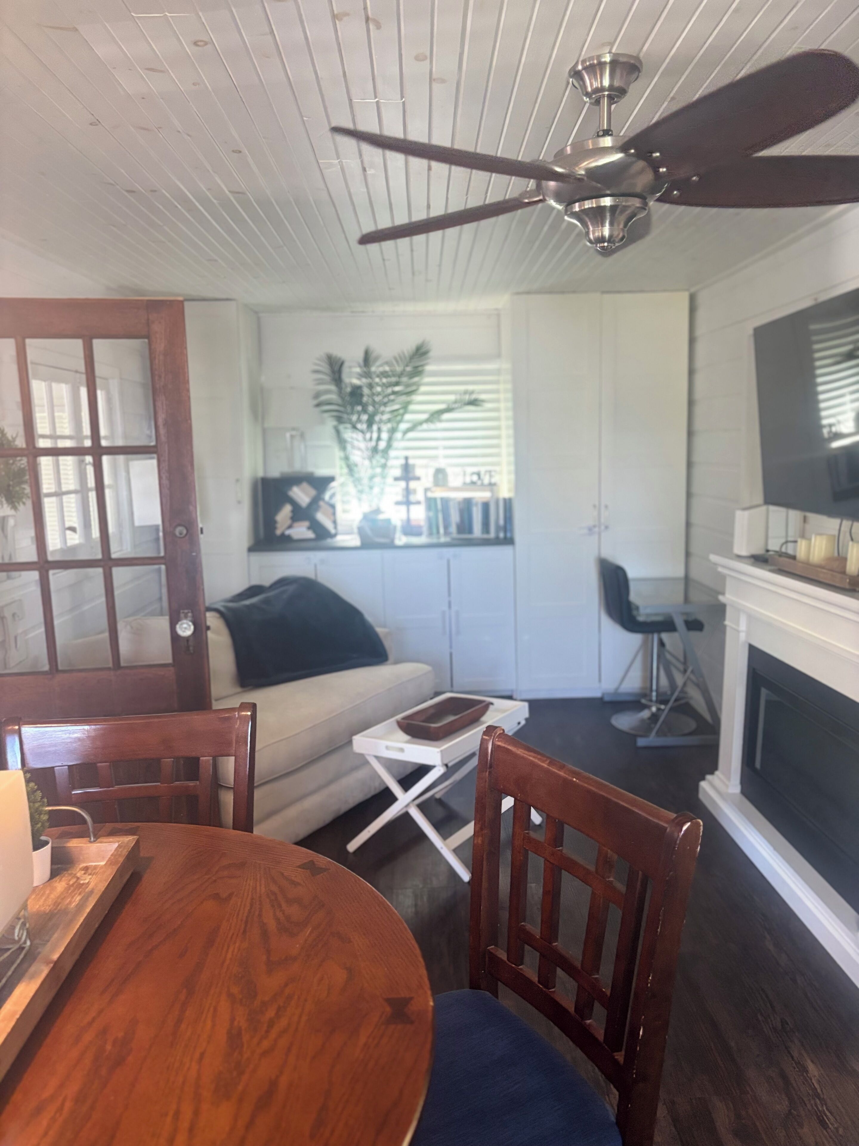 Un coin repas avec une table et des chaises en bois, un canapé blanc, un ventilateur de plafond et une cheminée.