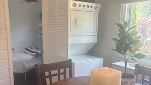 Ett rum med ett matbord i trä, en inbyggd tvättmaskin och torktumlare, en liten växt och ett fönster med utsikt över grönområden.