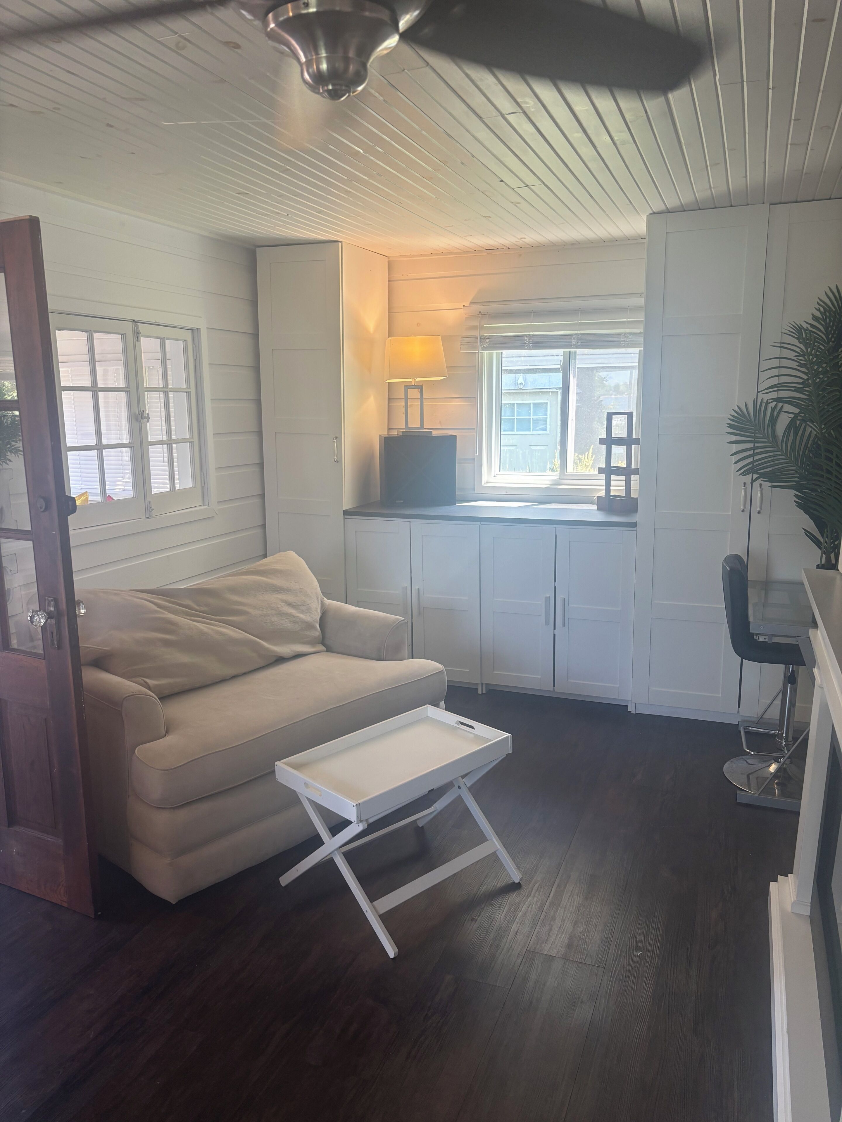 A room with a sofa, a small table, a lamp, a window, and a ceiling fan.
