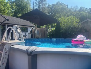 Ein oberirdischer Swimmingpool mit einer Leiter, einer überdachten Terrasse und aufblasbaren Spielzeugen.