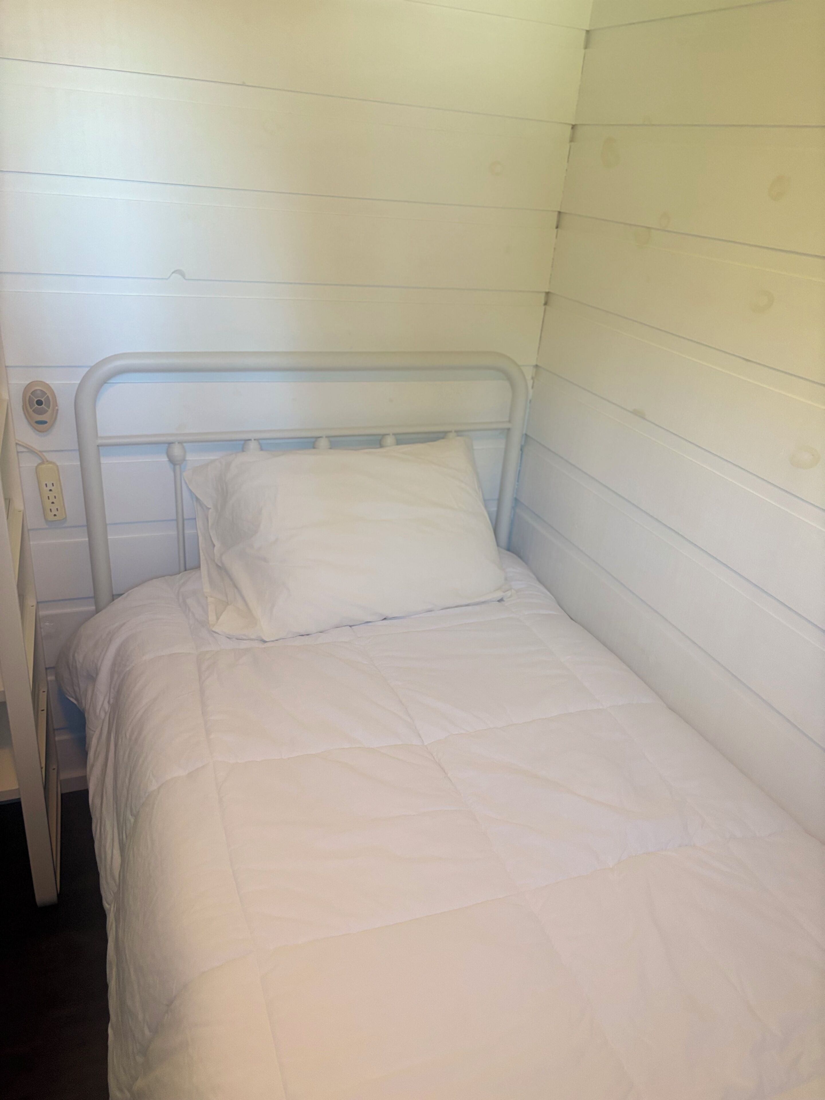 A single bed with a metal frame and white bedding in a room with white walls.