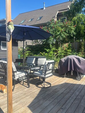 Eine Holzterrasse mit Gartenmöbeln, einem Grill und einer Pergola mit Sonnenschirm.