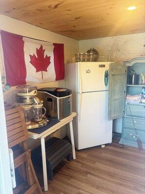 A compact kitchen with a white refrigerator, a blender, and a wooden table. - Siesta Pines Peaceful Retreat (Waubaushene)