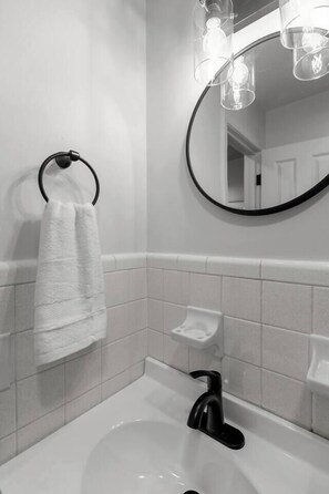 Un baño con lavamanos blanco, grifo negro y una toalla colgada en un aro negro.