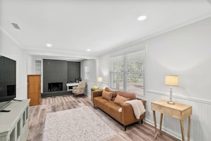 A living room with a fireplace, a sofa, a TV, and a lamp. - The Paddle House 3/2 Walking Distance To New Pickleball Courts (Dothan)