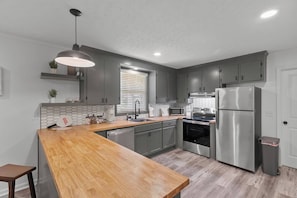 A modern kitchen with grey cabinets, stainless steel appliances, a wooden island, and a pendant light. - The Paddle House 3/2 Walking Distance To New Pickleball Courts (Dothan)