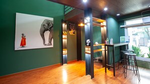 Una habitación con paredes verdes, suelo de madera, un cuadro grande de un elefante, una figurita de panda y una zona de bar con taburetes.