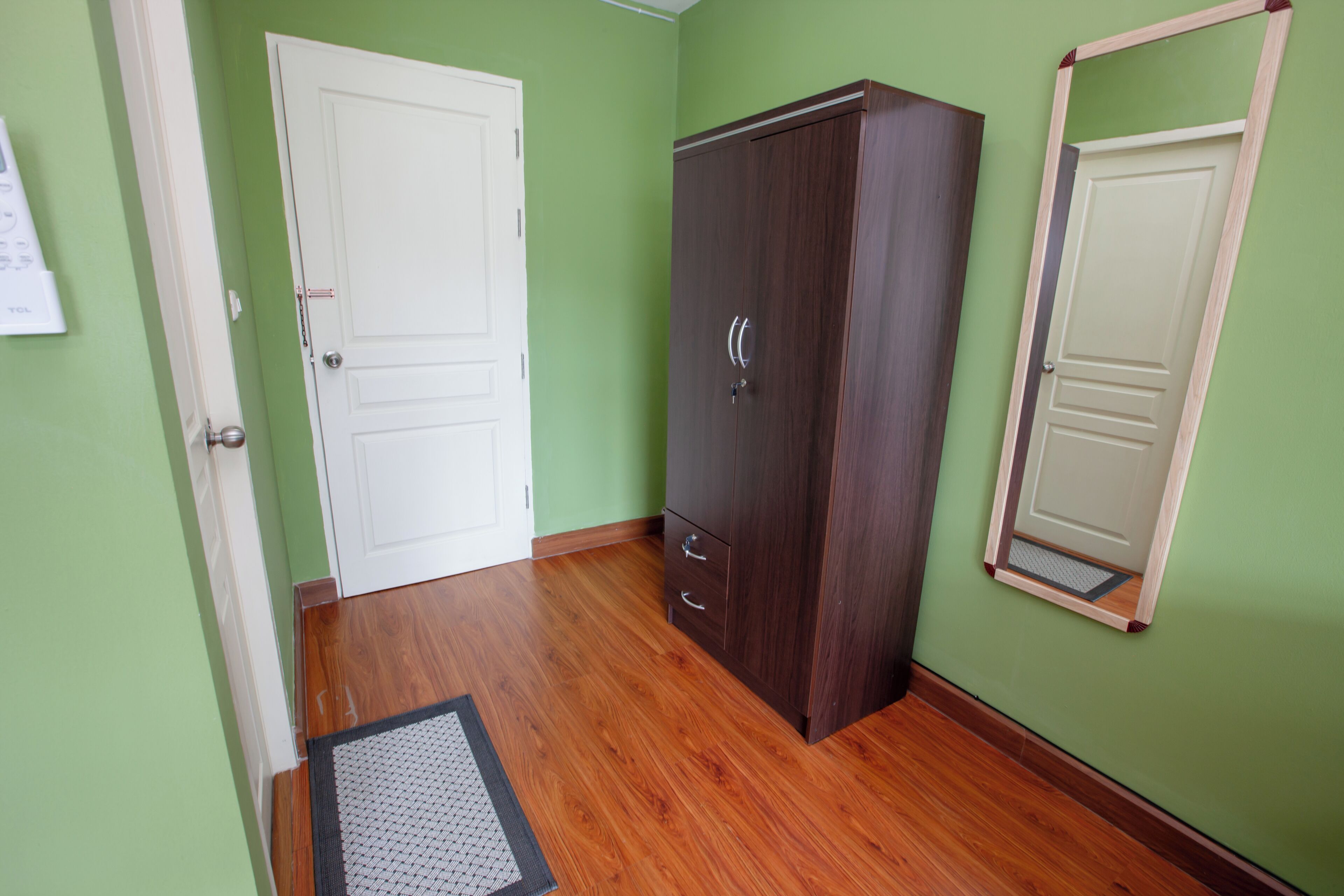 Une pièce avec un plancher en bois, une porte blanche, une armoire en bois foncé et un miroir au mur.