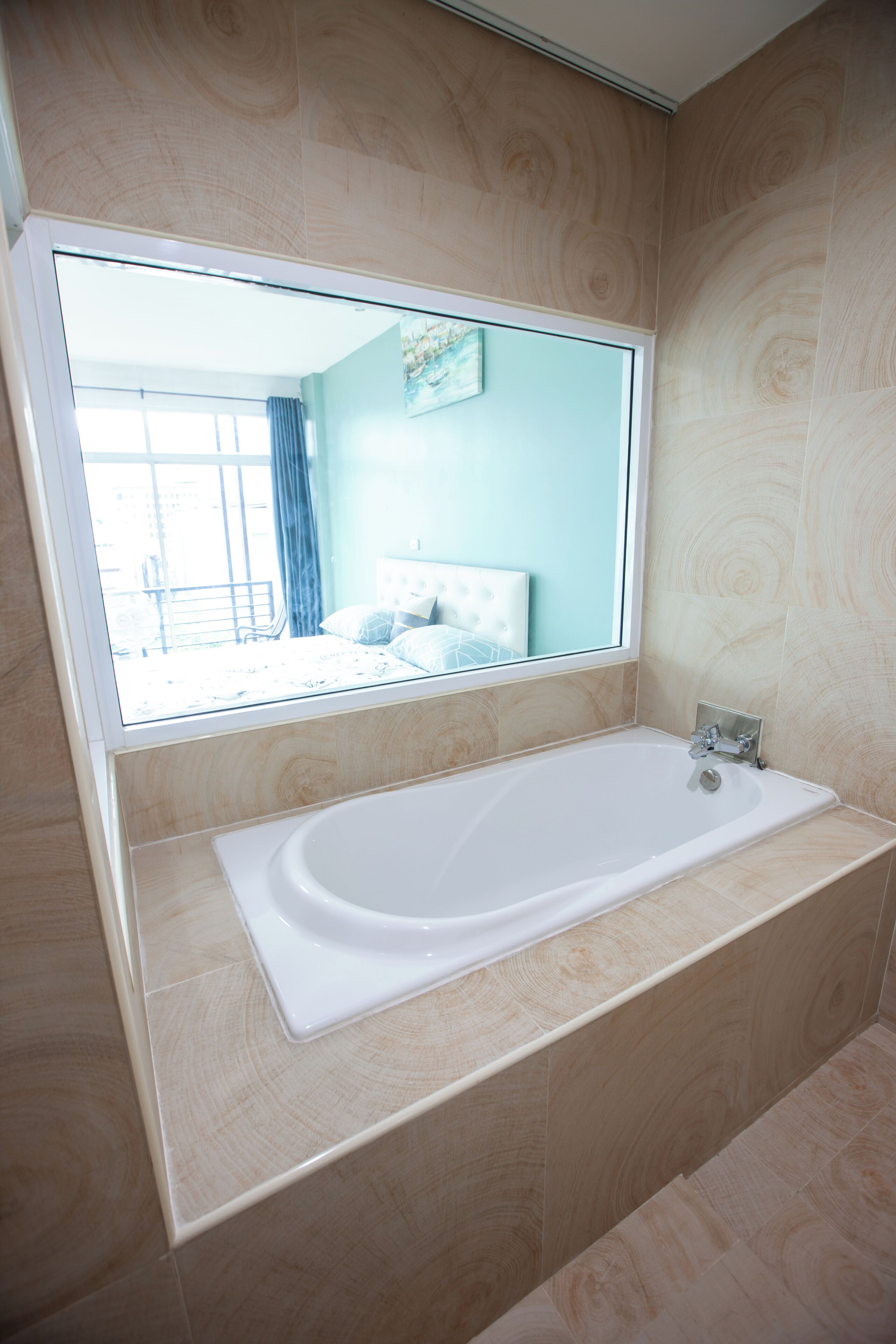 Ein modernes Badezimmer mit einem großen Spiegel, einer Badewanne und Blick auf ein Schlafzimmer durch das Fenster.