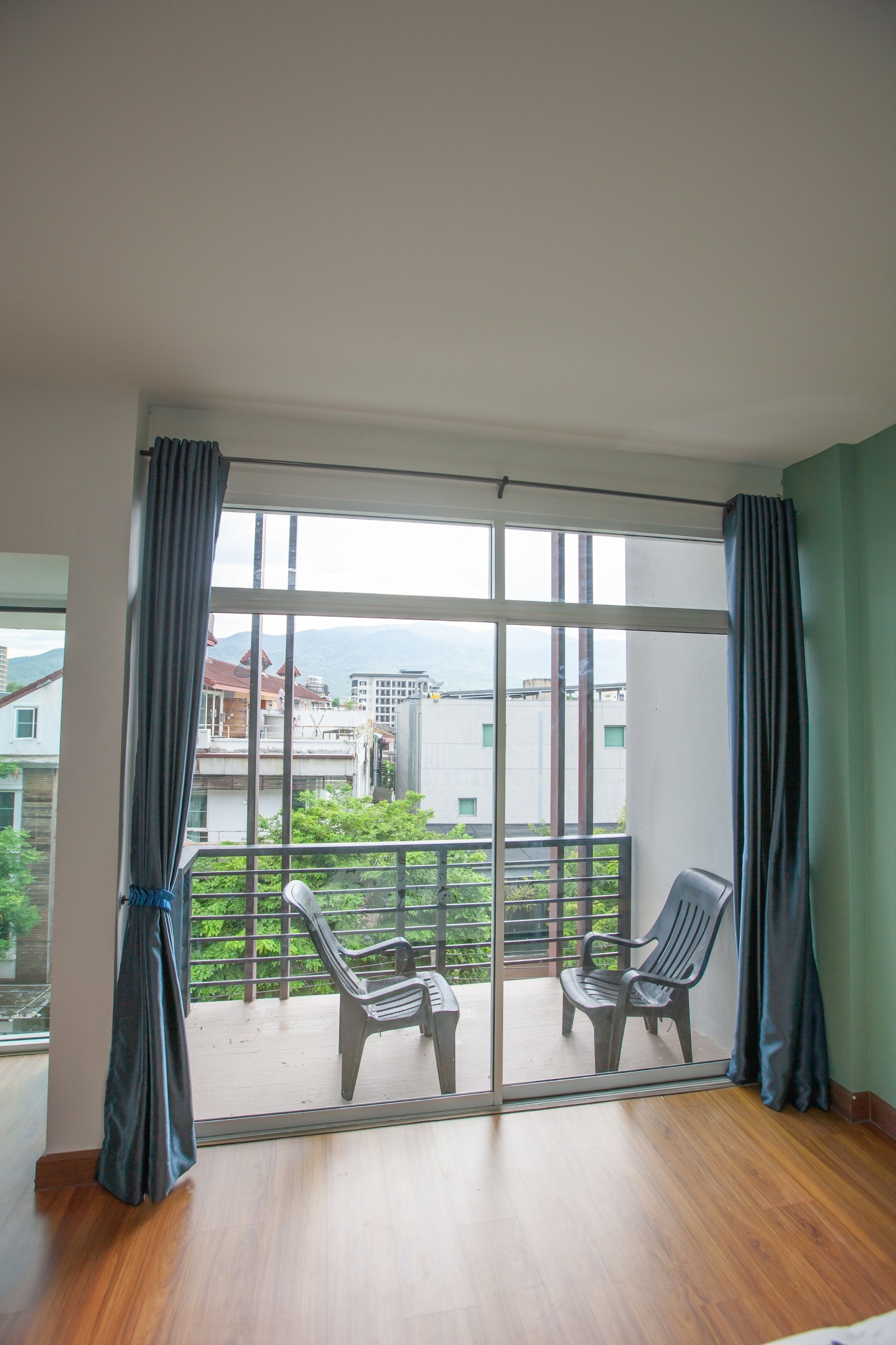 A room with a large sliding glass door leading to a balcony with two chairs and a view of buildings and greenery.