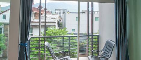 A room with a large sliding glass door leading to a balcony with two chairs and a view of buildings and greenery.
