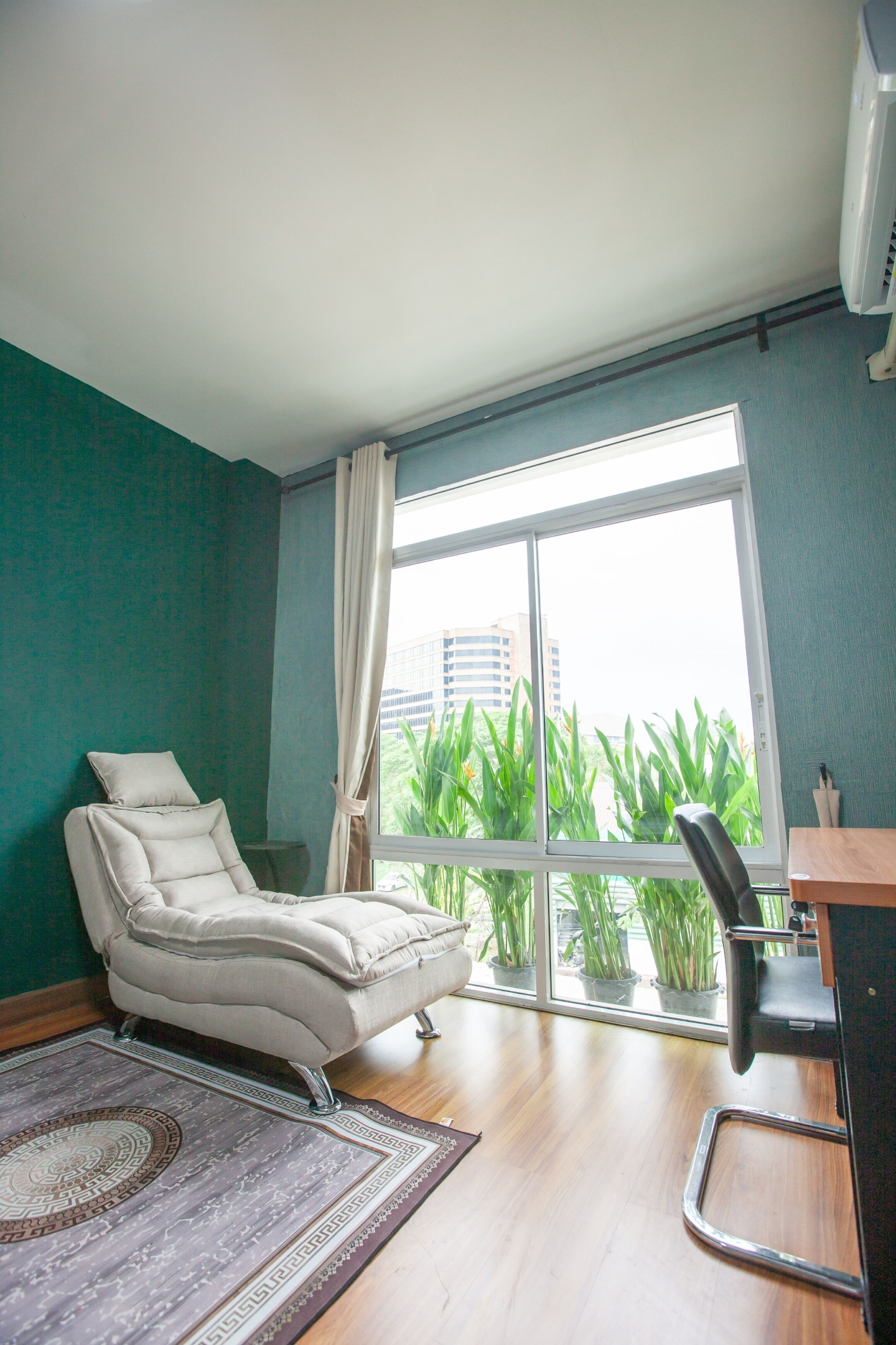 A room with a large window, a white chair, a desk, and a patterned rug.