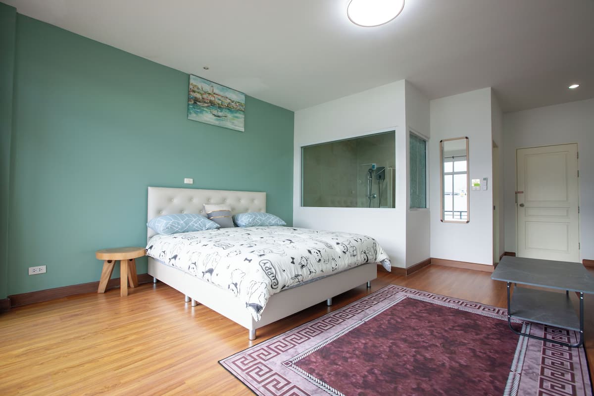 A bedroom with a bed, a small stool, a mirror, and a door.