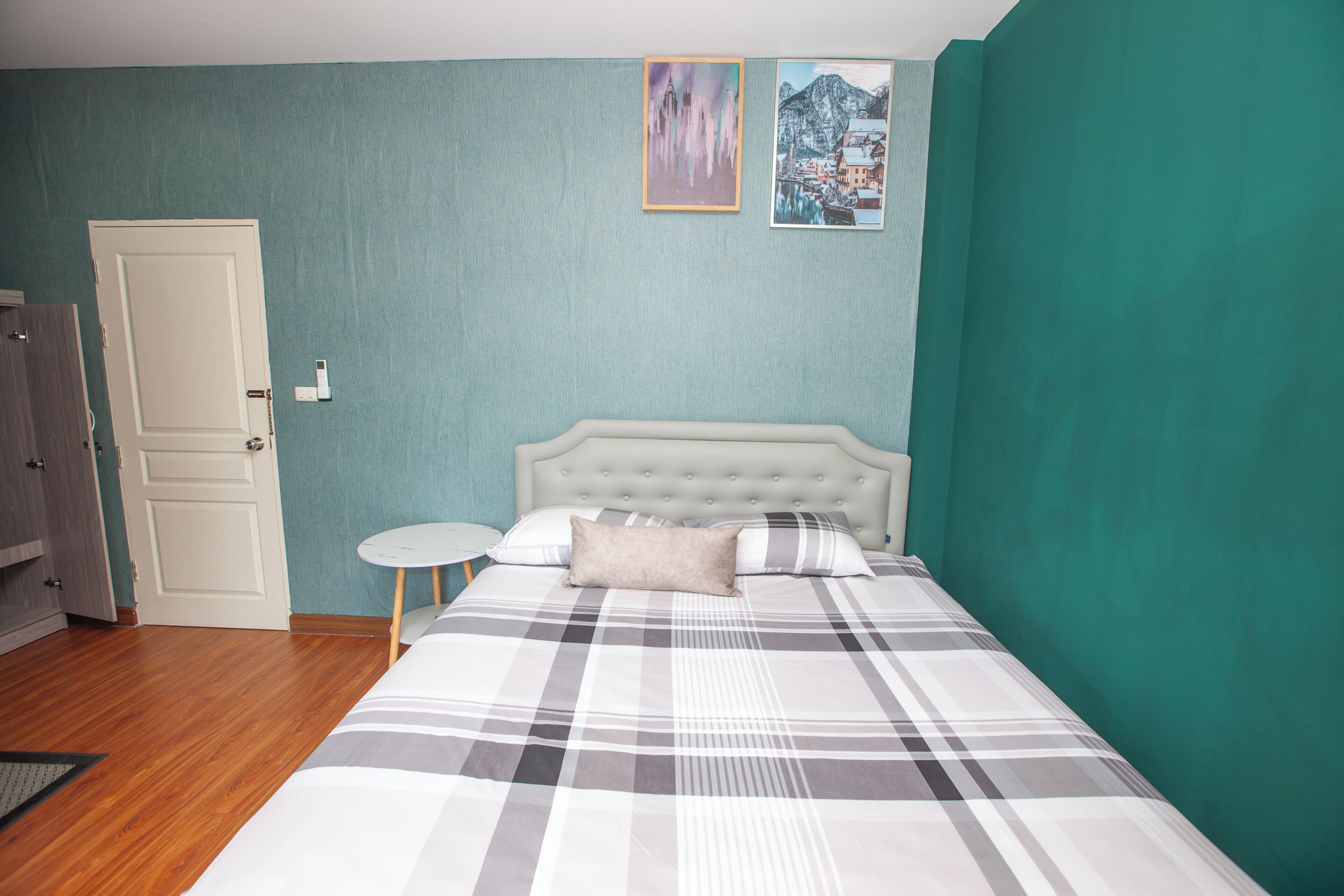 Un dormitorio con una cama, una puerta, una mesita redonda pequeña y dos cuadros en la pared.