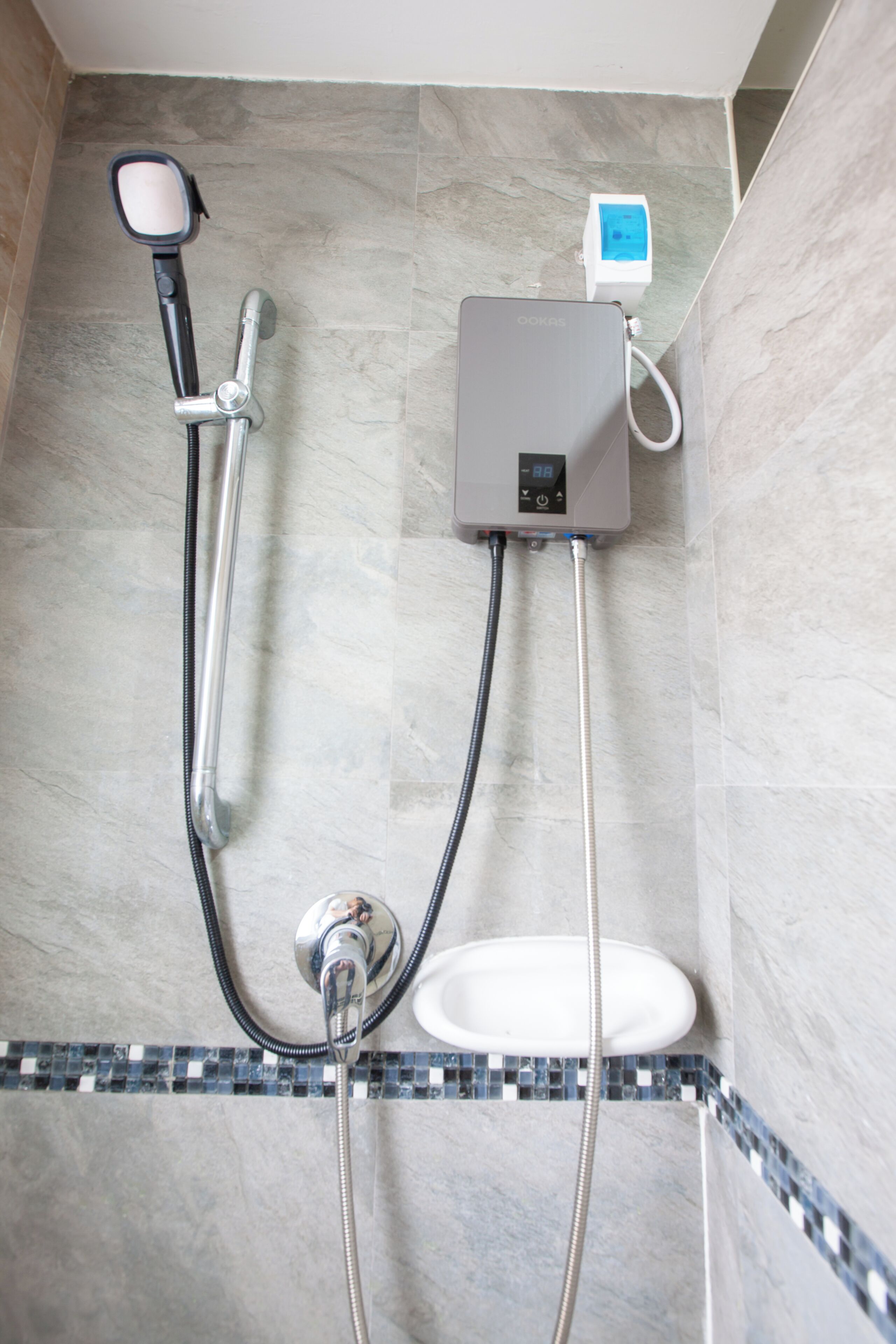 Une douche équipée d’un pommeau de douche à main, d’un panneau de commande mural et d’un lavabo blanc.