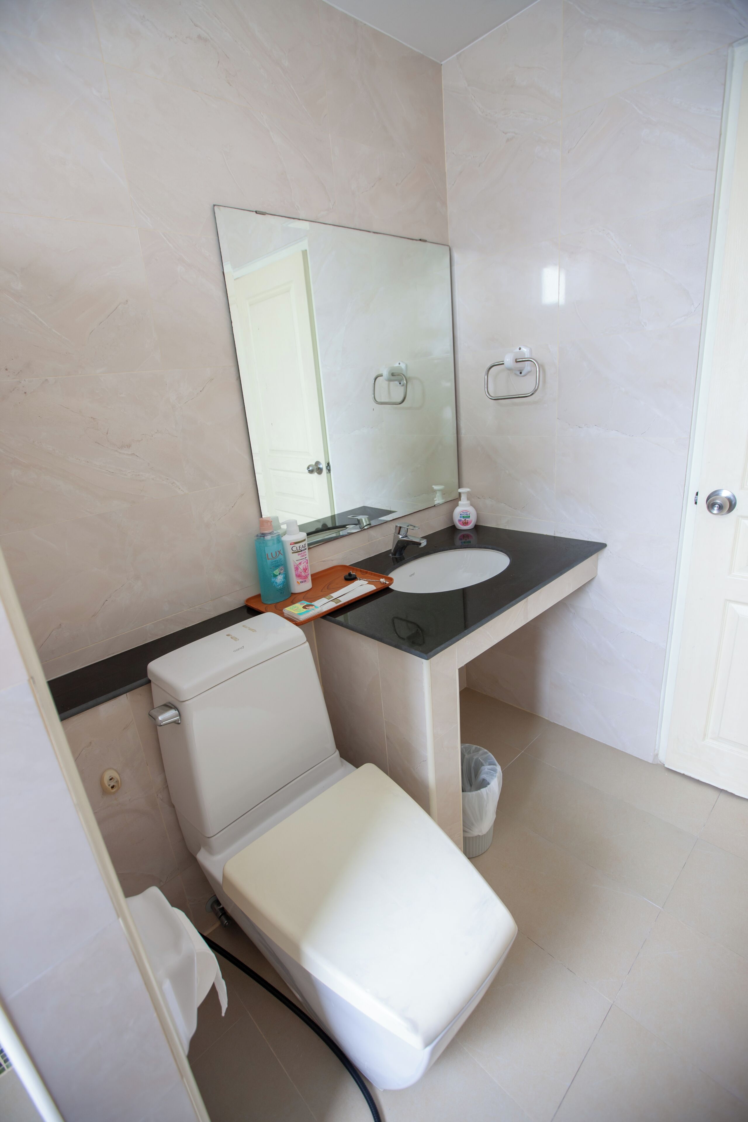 A bathroom with a toilet, sink, mirror, and a trash bin.